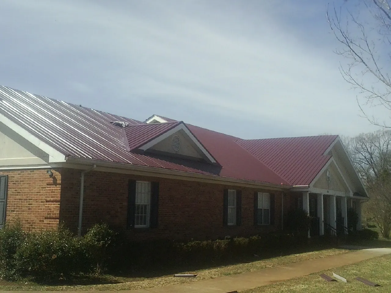 Red metal roof with gabled entries on a long brick building, from a Hail Damage Roof Repair job in Placida