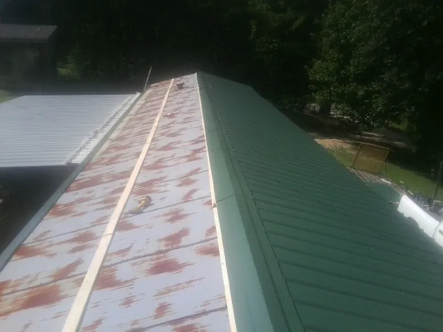 Old rusted panels beside newly installed green metal roofing — Wind Damage Roof Repair by Roofing Brothers in Placida