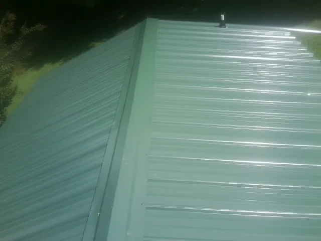 New green metal panels meeting at the ridge of a roof — Flat Roof Repair work by our crew in Placida