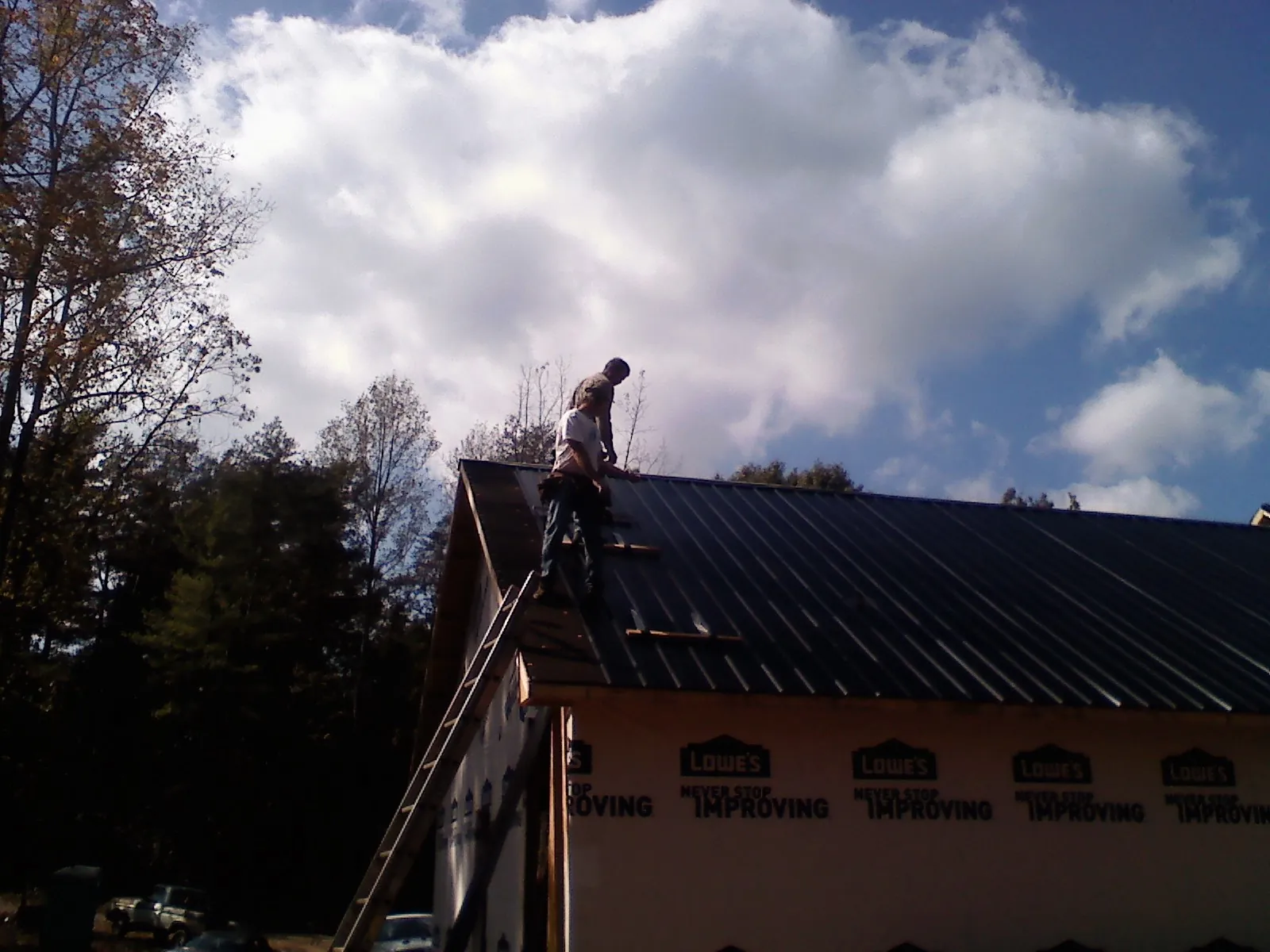 Roofer fastening dark metal panels high against a cloudy sky, from a Roof Inspection job in Placida