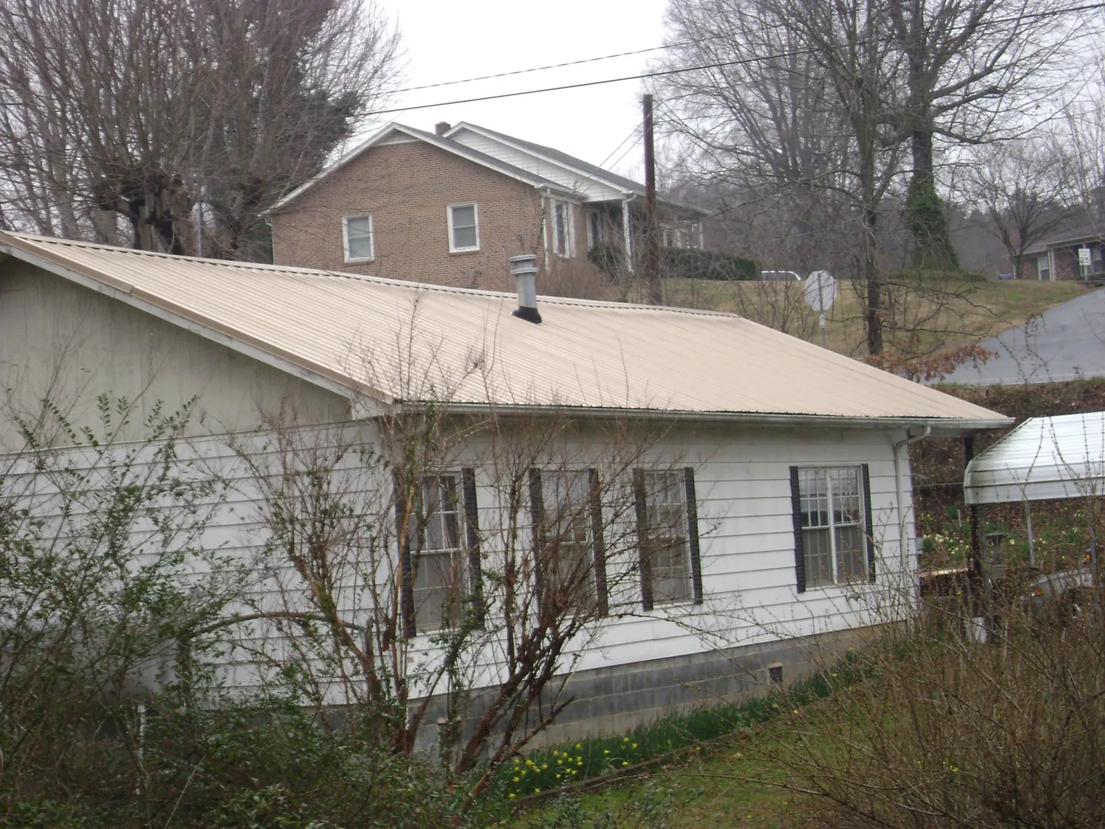 Tan metal roof on a white sided house set into a hillside — Commercial Roofing by Roofing Brothers in Placida